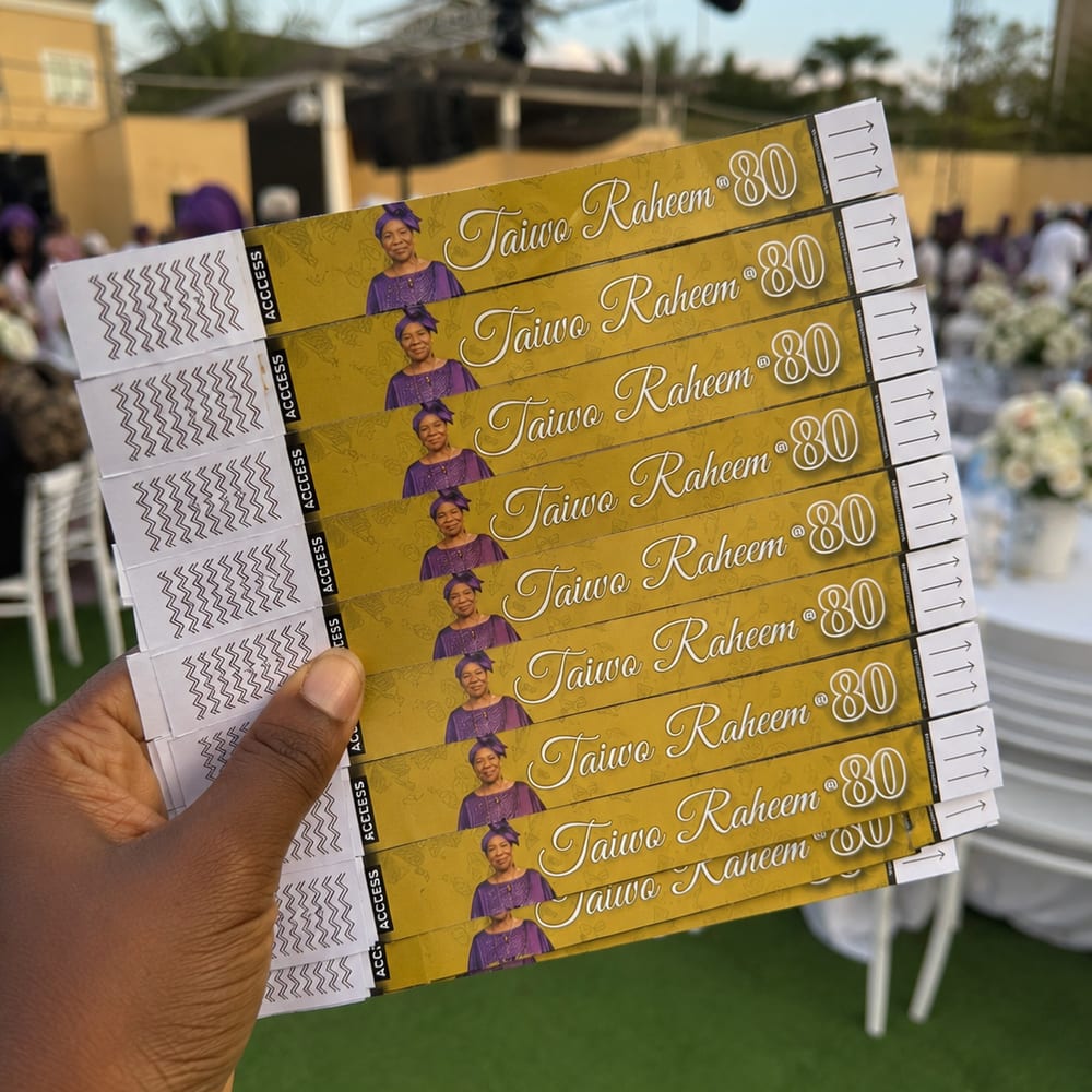 A fan of gold Taiwo Raheem @ 80 access wristbands held up at the venue, each printed with her portrait and a tear-off ACCESS tab